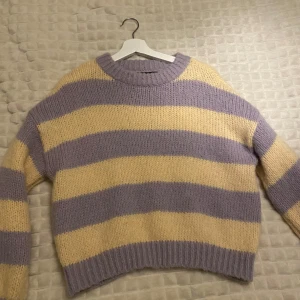 Randig stickad tröja från Vero Moda - Superfin stickad tröja från Vero Moda i lila och gul. Den har ett randigt mönster och är perfekt för kyliga dagar. Tröjan är croppad och har långa ärmar, vilket gör den både trendig och bekväm. Perfekt för höst och vinter! 🍂💜