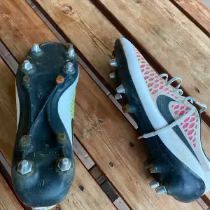 Säljer ett par Nike Mercurial fotbollsskor i välanvänt skick. Skorna har en cool design med röd och gul mesh på ovansidan och svarta detaljer. De har snörning och är perfekta för fotboll på gräsplaner med sina metallskruvdobbar. 