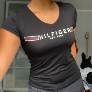 Svart t-shirt från Tommy Hilfiger - Säljer en snygg svart t-shirt från Tommy Hilfiger med deras ikoniska logga på bröstet. T-shirten har en v-ringad hals och korta ärmar, perfekt för en casual look. Den är i storlek S och sitter riktigt bra. Passar både till vardags och fest!