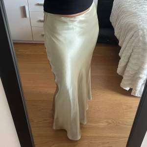 Säljer en superfin långkjol i en ljus beige färg. Kjolen är i satinmaterial vilket ger den en glansig look. Perfekt för festliga tillfällen eller när du vill känna dig extra elegant. Den har en smickrande passform och en diskret dragkedja på sidan!