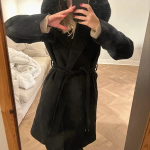 Sanne Alexandra kappa - Kappa i ull från Sanne Alexandra med luva med en fuskpäls på som går att ta av. Använd några fåtal gånger och i superfint skick. Jag är 166cm lång för referens