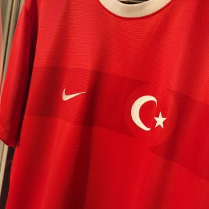 Nike TURKIEtS NATIONALLAG - Säljer en snygg röd fotbollströja från Nike med Turkiets flagga på bröstet. Tröjan är kortärmad och har en vit rund halsringning. Den är tillverkad i Dri-FIT-material som håller dig sval och torr under matchen.  100% Authentic 