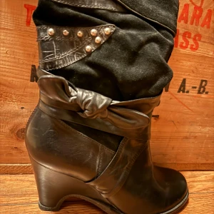 Svarta stövletter från Bronx - Säljer ett par snygga svarta stövletter från Bronx. De är i skinn med en cool snörning och nitar som detaljer. Klacken är stabil och ger en elegant look. Perfekta för höst och vinter, och funkar lika bra till vardags som till fest.