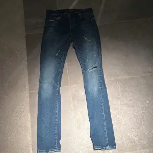 Säljer ett par snygga blå jeans med coola slitningar på framsidan. De har en klassisk femficksdesign och en bekväm passform. Perfekta för en avslappnad stil!