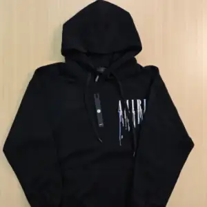 Säljer en snygg svart hoodie från Amiri med coolt tryck i flera färger på bröstet och ryggen. Den har en klassisk känguruficka och justerbar huva. Perfekt för en avslappnad stil eller att bära till vardags. Passar lika bra till jeans som till träningsbyxor.