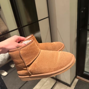 Bruna boots i mocka - Säljer ett par mysiga bruna boots i mocka. Perfekta för höst och vinter med sin varma insida. De har en enkel design utan snörning eller dragkedja, vilket gör dem lätta att ta på och av. Passar perfekt för en avslappnad stil.