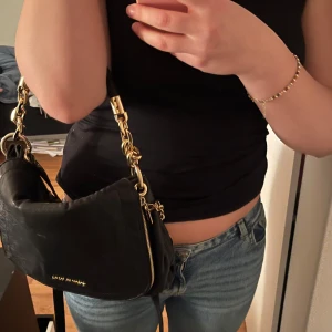 Svart axelväska från Michael Kors - Snygg svart axelväska i skinn från Michael Kors med gulddetaljer och dragkedja. Perfekt för både vardag och fest. Väskan har en praktisk storlek med flera fack inuti för enkel organisering. Tvek inte att kontakta eller tryck på köp dierekt!💗