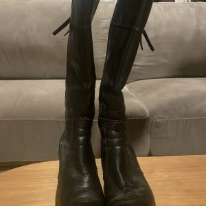 Svarta höga stövlar med snörning -  Jag säljer ett par Snygga svarta stövlar i skinn med hög skaft och dragkedja på sidan. Jag köpte de till min syster för 1000 kr hon har andvämt de 5 gånger  men nu är de tyvärr för små. De har en cool snörningsdetalj baktill. De är i storlek 35 