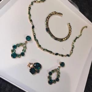 Grön smyckeset med örhängen, halsband, armband och ring - Säljer ett elegant smyckeset med gröna stenar. Setet inkluderar ett par örhängen, ett halsband, ett armband och en ring. Perfekt för festliga tillfällen! 💚aldrig använd,nypris 5000kr
