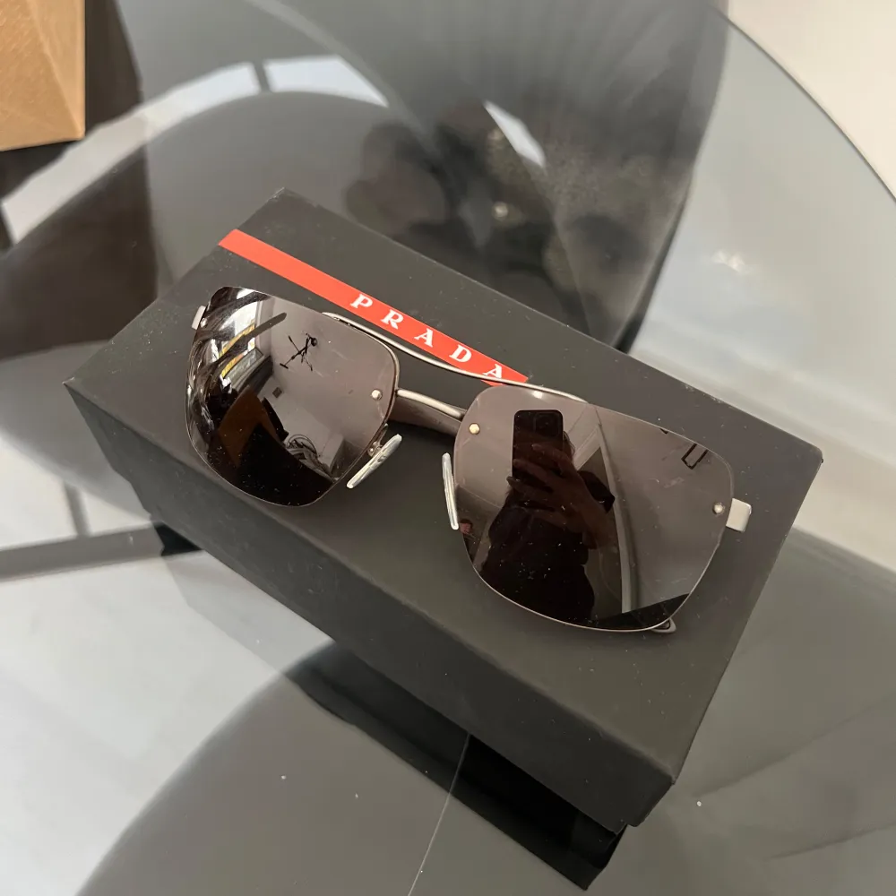 Säljer ett par snygga solglasögon från Prada i mycket bra skick. De har en modern design med mörka glas och en stilren metallram. Perfekta för både sommar och vår, och ger en lyxig touch till vilken outfit som helst. Kommer med originalförpackning. Köpta för 3500kr.. Asusteet.