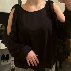 Svart blus med öppna axlar - Säljer en elegant svart blus med öppna axlar och långa ärmar. Blusen har en lös passform och är perfekt för både vardag och fest. Materialet är mjukt och bekvämt, vilket gör den skön att bära hela dagen. Passar bra till både jeans och kjol!