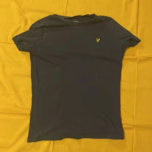 Svart t-shirt från Lyle & Scott - Säljer en stilren svart t-shirt från Lyle & Scott med deras ikoniska gula logga på bröstet. T-shirten är i bra skick och har en normal passform. Perfekt för vardagsbruk eller en avslappnad dag ute. Passar till allt och är superbekväm!