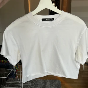 Croppad t-shirt - Vit croppad t-shirt från Bikbok, bara använd någon enstaka gång. Längd på tröjan ca 38 cm