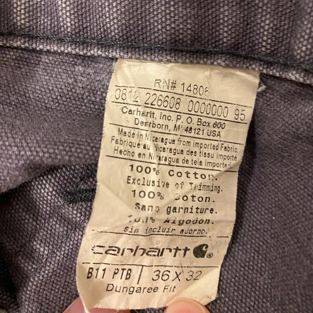 Säljer ett par grå Carhartt byxor i Dungaree Fit. De är tillverkade i 100% bomull och har en avslappnad passform med flera praktiska fickor. Perfekta för vardagsbruk eller arbete. Byxorna är i bra skick och redo för nya äventyr!. Farkut & Housut.
