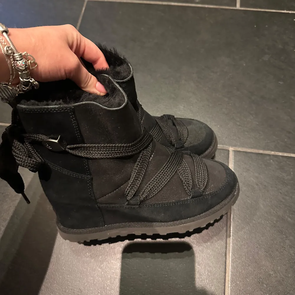 Säljer ett par svarta UGG i mycket bra skick. De har en mysig pälsfodring inuti och robusta sulor för bra grepp. Skorna har snörning baktill för en justerbar passform. Dom har en liten kilklacka. Perfekta för kalla vinterdagar! Använda 1 gång, fin och unik model.. Kengät.