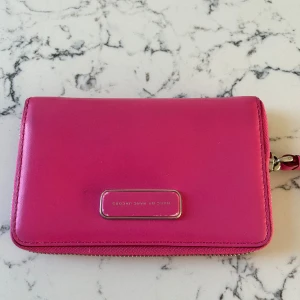 Rosa plånbok från Marc by Marc Jacobs - Säljer en snygg rosa plånbok från Marc by Marc Jacobs i mycket bra skick. Den har en praktisk dragkedja och flera fack för kort och ID. Perfekt för att hålla ordning på dina saker med stil! 💖