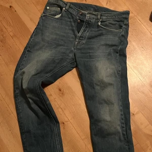 Blå jeans från J.Lindeberg storlek 32 - Säljer ett par snygga blå jeans från J.Lindeberg i bra skick. De har en klassisk femficksdesign och knappar i midjan. Perfekta för både vardag och fest. Passar bra till en casual look eller med en skjorta för en mer uppklädd stil.