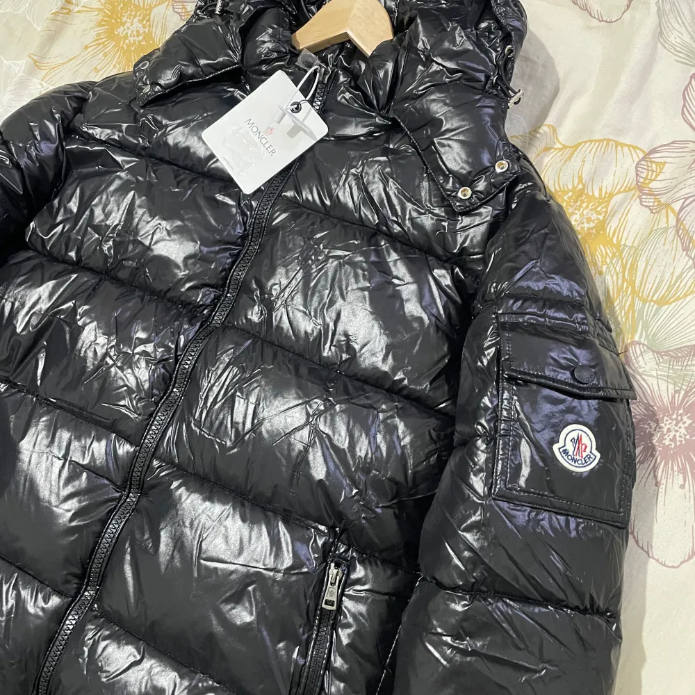 Säljer en snygg svart dunjacka från Moncler i nytt skick. Jackan är pufferstil med en glansig finish och har en praktisk dragkedja framtill. Den är långärmad och perfekt för vintern. Storleken är inte specificerad, men den ser ut att vara normal passform. Perfekt för att hålla sig varm och stilren i kylan!. Jackor.