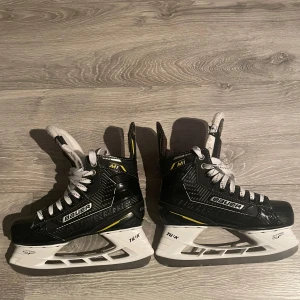 Svarta skridskor från Bauer - Säljer ett par svarta Bauer Supreme skridskor i mycket bra skick. De har en snygg design med vita snören och gula detaljer. Perfekta för vinterns isäventyr! 🏒 St 4 (37.5) 