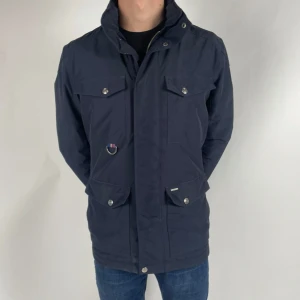 Mörkblå jacka från Snoot - Säljer en stilren mörkblå jacka från Snoot i storlek M. Jackan har långa ärmar och flera praktiska fickor med knappar. Perfekt för höst och vår med sitt quiltade foder som håller dig varm. Dragkedja och knappar framtill för extra skydd mot kyla.