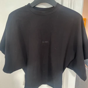 Svart t-shirt från Avora - Säljer en stilren svart t-shirt från Avora. Den har en enkel design med rund hals och korta ärmar. Perfekt för en avslappnad look eller som basplagg i garderoben. Passar till allt!