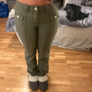 Lågmidjade utsvängda byxor  - Säljer ett par olivgröna byxor från H&M Divided i storlek 38. Byxorna har en normal passform med knappar och fickor fram. Perfekta för höst och vår, och de är i mycket bra skick. Säljs inte längre på hm! 