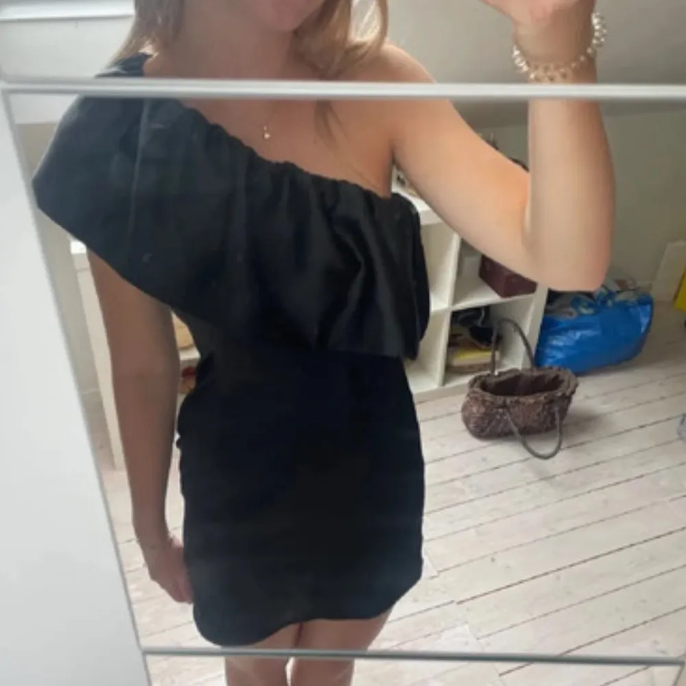 Snygg svart oneshoulder klänning med volangdetalj. Perfekt för festliga tillfällen! Klänningen är kort och har en tight passform som framhäver figuren. Materialet är i satin. Skriv för fler bilder🖤. Klänningar.