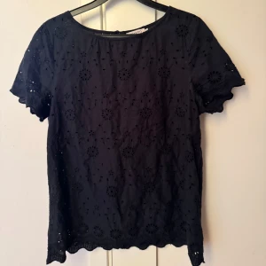 Svart blus från Soaked in Luxury - Snygg svart blus från Soaked in Luxury i storlek M. Blusen har ett fint broderat mönster och korta ärmar. Perfekt för både vardag och fest! 🖤