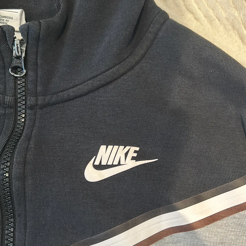 Säljer en grå svart Nike tech flece. Den är väldigt sunki så det blir väldigt lågt pris. Det är storlek 147-158cm. Hoodies.