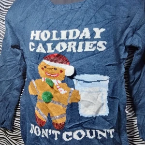Blå jultröja med pepparkaksgubbe - Säljer en rolig blå jultröja med texten 'Holiday Calories Don't Count' och en pepparkaksgubbe med tomteluva. Perfekt för julfesten eller mysiga vinterkvällar. Tröjan har långa ärmar och är gjord i ett mjukt material.