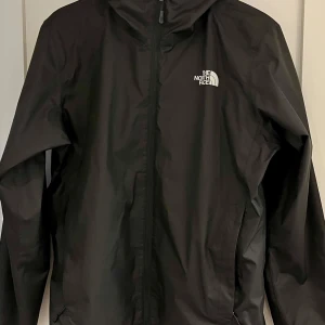 OANVÄND Svart vindjacka North Face  - Säljer en svart vindjacka från The North Face i storlek S. Jackan har en dragkedja framtill och är perfekt för höst och vår. Den är i mycket bra skick och har en klassisk stil med The North Face-loggan på bröstet och ryggen. Perfekt för utomhusaktiviteter eller vardagsbruk! Helt fleckfri, oanvänd. Nypris - 1300 så se det som en 500 kr rabatt