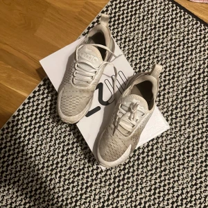 Beige Nike Air Max 270 - Säljer ett par snygga och bekväma Nike Air Max 270 i beige. De har en luftig design med snörning och en synlig Air-enhet i hälen för extra komfort. Perfekta för både vardag och träning. Skorna är i bra skick och redo för nya äventyr!