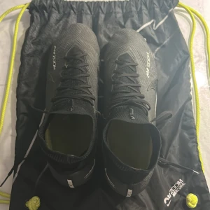 Nike mercurial fotbollskor - Säljer ett par svarta fotbollsskor i mycket bra skick. De har en snygg design med snörning och Zoom-sula för extra grepp på planen. Perfekta för fotbollsträning eller match. Kommer med en praktisk svart gympåse med gula snören. Säljs pågrund av att de är för små priset är så pass lågt för behöver verkligen få sålt skorna bara därför inga problem på skor inte skador eller liknade 
