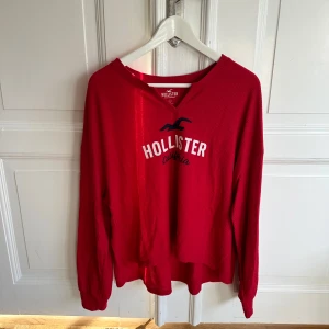 Röd långärmad tröja från Hollister - Säljer en snygg röd långärmad tröja från Hollister med deras ikoniska logga på bröstet. Perfekt för en avslappnad stil och passar bra till både jeans och shorts. Tröjan är i bra skick och redo för nya äventyr!