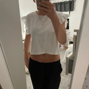 Vit croppad topp med volangärmar - Säljer en söt vit croppad topp med volangärmar. Perfekt för sommardagar eller en avslappnad fest. Toppen är i ett lätt och bekvämt material, vilket gör den idealisk för varma dagar. Passar bra till både jeans och kjol!