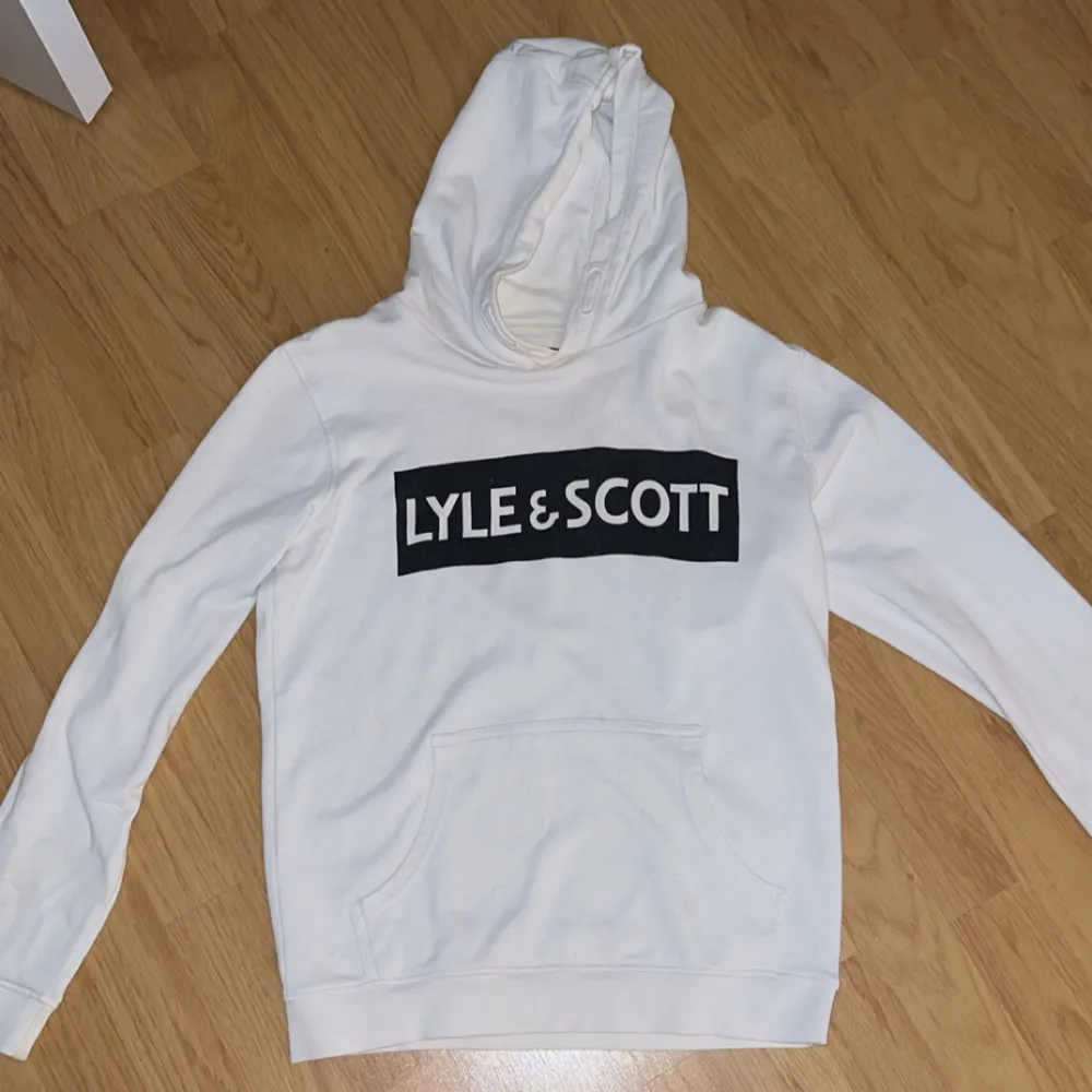 Säljer en snygg vit hoodie från Lyle & Scott. Den har en stor logga på bröstet och en klassisk känguruficka. Perfekt för en avslappnad stil och passar till alla årstider. Skön och stilren design!. Tröjor & Koftor.