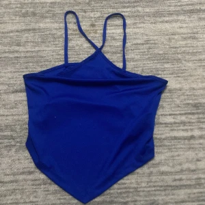 Blå linnetopp från Gina Tricot - Snygg blå linnetopp från Gina Tricot i storlek S. Perfekt för sommardagar med sin enkla och stilrena design. Toppen har smala axelband och en asymmetrisk nederkant som ger en unik look.