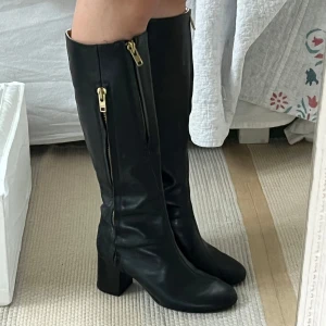 Svarta stövlar från Acne - Snygga svarta stövlar i skinn från Acne Studios med dragkedja i guld på sidan. De har en klack som ger lite extra höjd och stil, och en snygg sömndetalj över foten. Perfekta för höst och vinter, och funkar lika bra till vardags som till fest. Stövlarna är i mycket bra skick och kommer med orginalpåse.