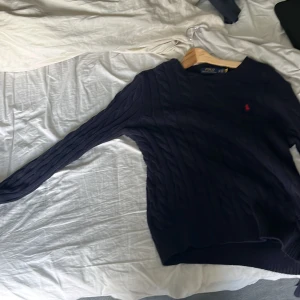 Mörkblå stickad tröja från Ralph Lauren - Säljer en snygg mörkblå stickad tröja från Ralph Lauren. Den har ett klassiskt kabelstickat mönster och en liten röd logga på bröstet. Tröjan är långärmad och perfekt för höst och vinter. Den är i storlek Xs men passar 100% M om inte större