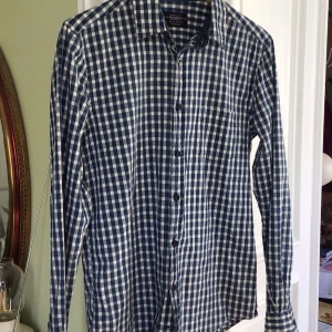Blå och vit rutig skjorta från Pull&Bear - Säljer en snygg blå och vit rutig skjorta från Pull&Bear. Skjortan har långa ärmar och knappar hela vägen ner. Perfekt för både vardag och fest! 🕺