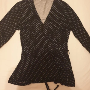 Blus - Snygg blus med v-ringning och långa ärmar. Blusen har ett mönster med små blommor och en snörning i midjan. Säljer för 50