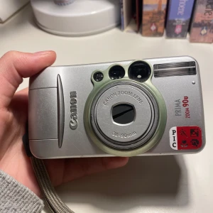 Film Kamera - Säljer en digital kamera! Model: Canon Prima Zoom 90u. Fungerande men medkommer ej film eller sladd💕 Skriv för fler bilder eller vid frågor! Är öppen för prisförslag. Säljer även två andra kameror🫶