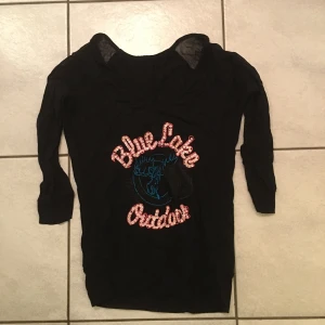 Svart tröja med tryck från Blue Lake - Snygg svart tröja från Blue Lake med ett färgglatt tryck på framsidan. Tröjan har trekvartsärmar och en bekväm passform. Perfekt för en avslappnad stil.