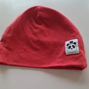 Röd mössa Mini Rodini - Snygg röd mössa från Mini Rodini med ett gulligt panda-märke framtill. Perfekt för att hålla värmen med stil.