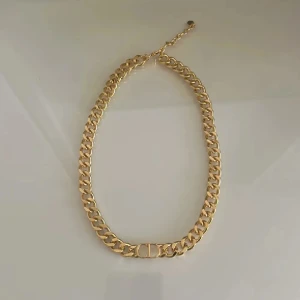 Guldhalsband med kedjedesign - Elegant guldhalsband med en klassisk kedjedesign och ett dekorativt 'CD'-emblem i mitten. Perfekt för att ge en lyxig touch till din outfit.