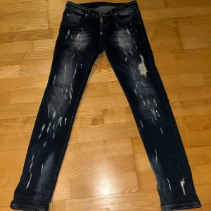 Mörkblå jeans från Dsquared2 - Snygga mörkblå jeans från Dsquared2 med slitna detaljer och en cool vintage-look. De har en knappgylf och klassisk femficksdesign. Perfekta för en avslappnad stil med en touch av edge.
