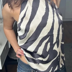 Zebramönstrad topp  - Säljer en supercool zebramönstrad blus i svart och beige. Den har en snygg, slät yta och är perfekt för en utekväll eller fest. Första bilden är lånad och toppen har prislappen kvar.