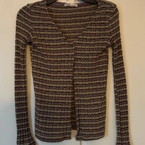 Randig långärmad tröja  - Snygg och stilren randig tröja från Pull and Bear. Tröjan har en v-ringad design och långa ärmar, perfekt för både höst och vår. Den är i en mix av jordnära färger som brunt och beige.