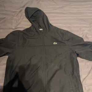 Svart tracksuit från Lacoste - Snygg svart tracksuit från Lacoste med elastisk midja och det ikoniska krokodilmärket på bröstet och benet. Perfekta för en sportig look eller avslappnade dagar. Ny pris 2600kr