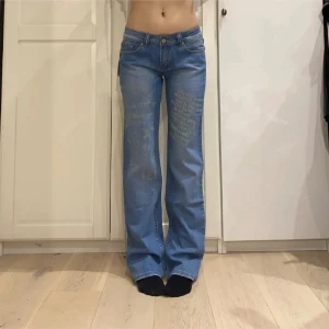 Blå jeans med broderad text - Snygga blå jeans med broderad text på både fram- och baksida. De har en klassisk femficksdesign och en rak passform som ger en avslappnad look. Perfekta för dig som vill ha något unikt i garderoben!